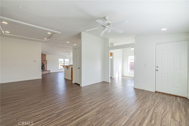 unfurnished living room with dark wood-type flooring, ceiling fan, lofted ceiling, and a stone fireplace