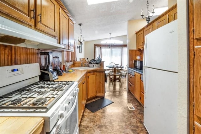 kitchen featuring lofted ceiling, an inviting chandelier, kitchen peninsula, pendant lighting, and white appliances