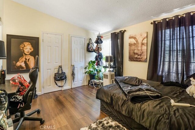 bedroom featuring hardwood / wood-style flooring, vaulted ceiling, and a textured ceiling