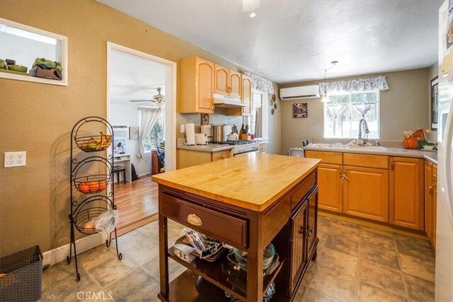 kitchen with sink, hanging light fixtures, stove, ceiling fan, and a wall unit AC