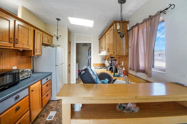 kitchen with pendant lighting, butcher block counters, lofted ceiling with skylight, white refrigerator, and a textured ceiling