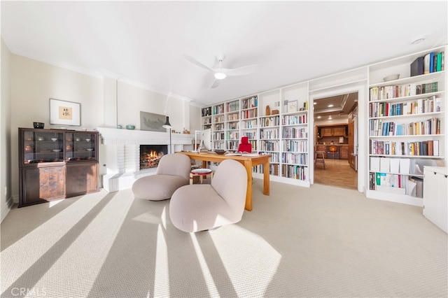 sitting room featuring light carpet, a brick fireplace, crown molding, and ceiling fan