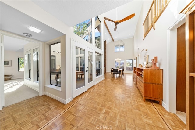 hallway featuring light parquet flooring, a towering ceiling, a notable chandelier, and french doors