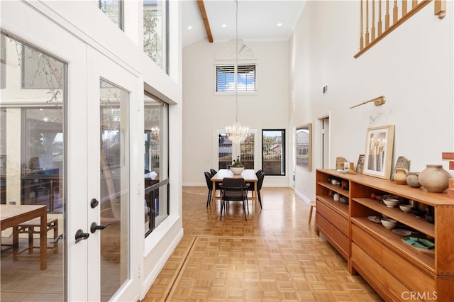 interior space featuring a towering ceiling, beamed ceiling, light parquet floors, an inviting chandelier, and french doors