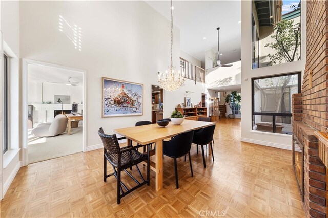 dining room featuring light parquet flooring, ceiling fan with notable chandelier, and a high ceiling