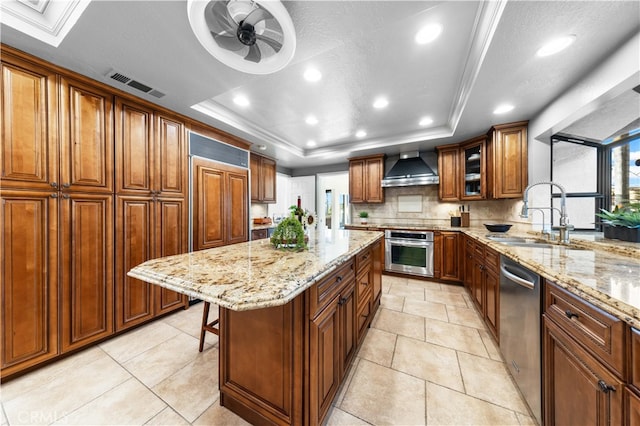 kitchen featuring wall chimney exhaust hood, sink, a center island, a tray ceiling, and stainless steel appliances