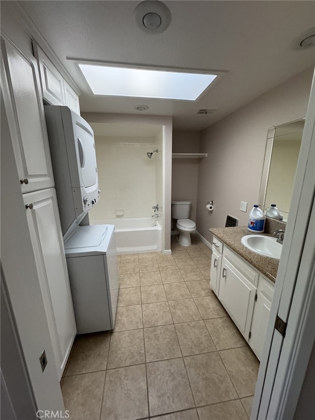 full bathroom featuring a skylight, stacked washer / dryer, vanity, toilet, and tile patterned floors