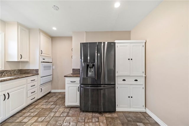 kitchen with white cabinets, oven, dark stone countertops, and stainless steel fridge