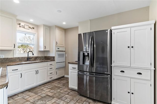 kitchen with sink, stainless steel fridge with ice dispenser, white oven, and white cabinets