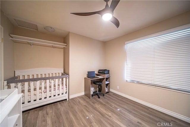 bedroom with hardwood / wood-style flooring, a nursery area, and ceiling fan