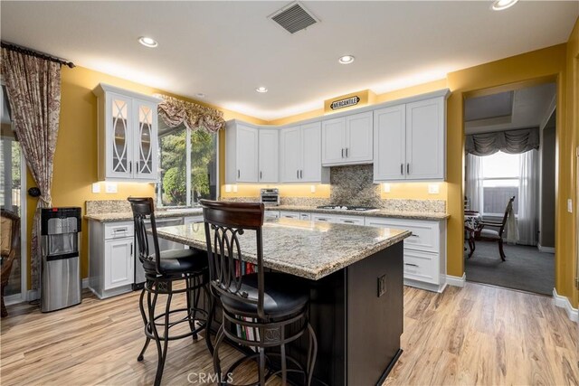 kitchen featuring a kitchen island, a breakfast bar area, white cabinets, light stone counters, and light wood-type flooring