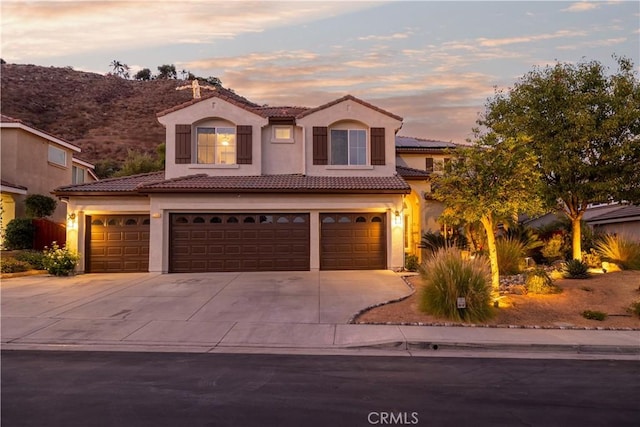 mediterranean / spanish house with stucco siding, concrete driveway, a garage, a tile roof, and roof mounted solar panels