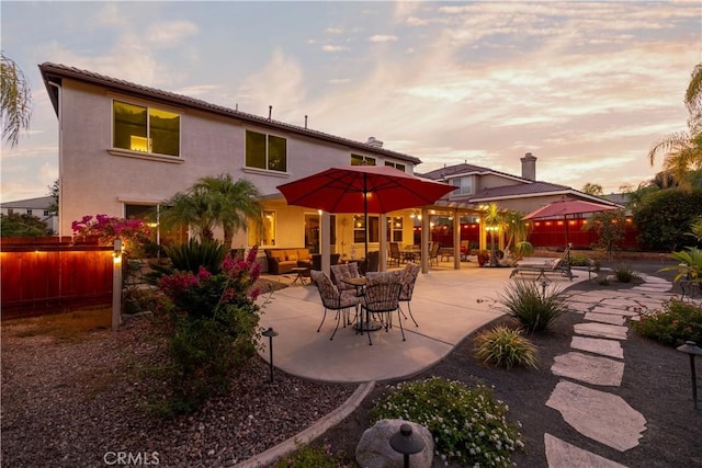 back house at dusk with an outdoor living space and a patio area