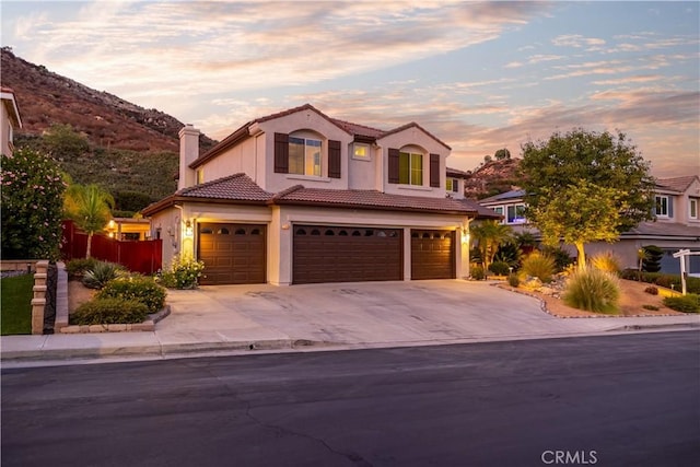 view of front of property with an attached garage, a chimney, stucco siding, concrete driveway, and a tiled roof