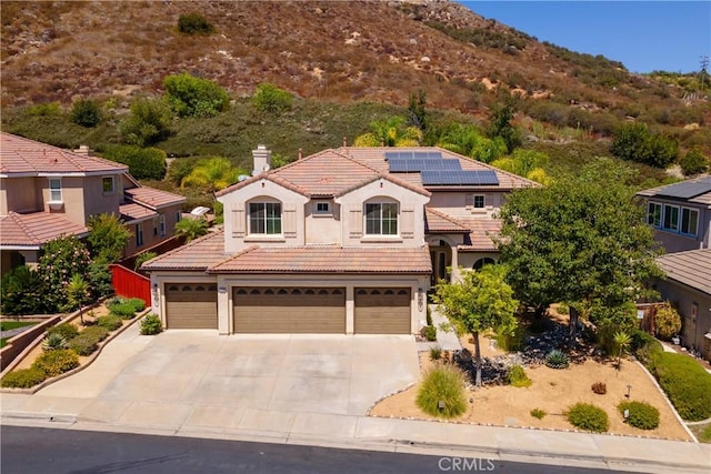 mediterranean / spanish house with stucco siding, driveway, a tile roof, a garage, and a chimney