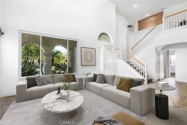 living area featuring baseboards, stairs, a towering ceiling, wood finished floors, and arched walkways