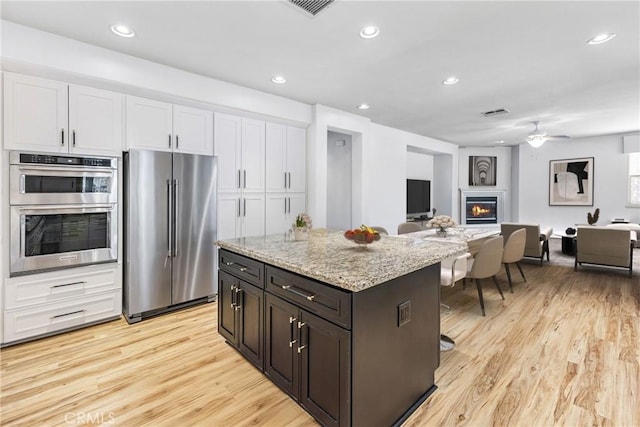 kitchen with light wood-type flooring, a glass covered fireplace, open floor plan, stainless steel appliances, and white cabinets