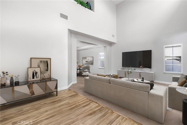 living room with visible vents, a high ceiling, baseboards, and wood finished floors