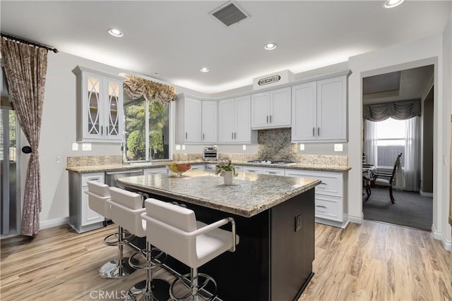 kitchen with tasteful backsplash, visible vents, a center island, a breakfast bar area, and light wood-style floors