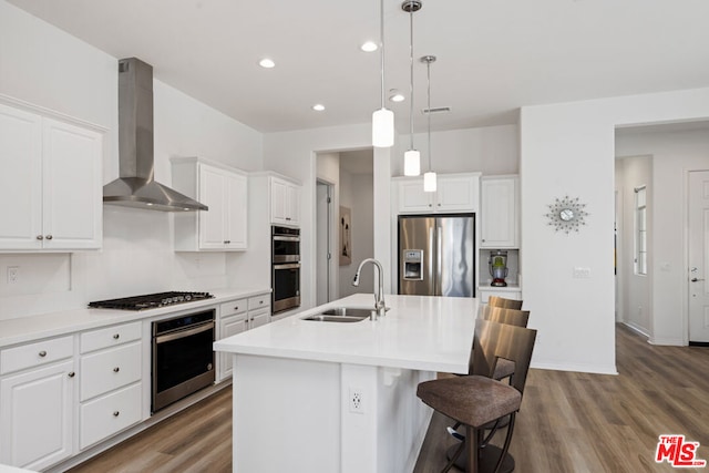 kitchen with an island with sink, appliances with stainless steel finishes, sink, and wall chimney exhaust hood