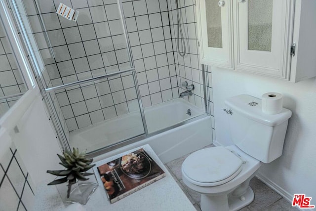 bathroom featuring tile patterned flooring, bath / shower combo with glass door, and toilet