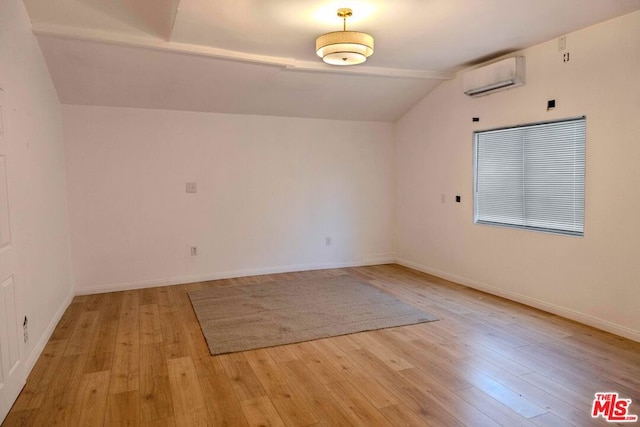 spare room featuring vaulted ceiling, an AC wall unit, and light hardwood / wood-style floors