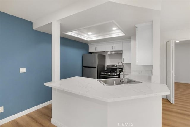 kitchen with appliances with stainless steel finishes, a tray ceiling, white cabinets, kitchen peninsula, and light wood-type flooring