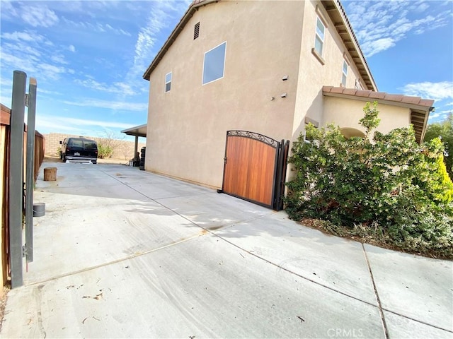 view of side of home with driveway, fence, a gate, and stucco siding