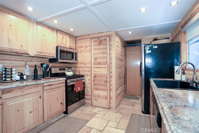 kitchen with sink, wooden walls, light brown cabinets, and appliances with stainless steel finishes