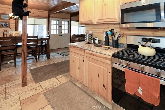 kitchen featuring appliances with stainless steel finishes, wooden walls, light brown cabinetry, wooden ceiling, and beamed ceiling