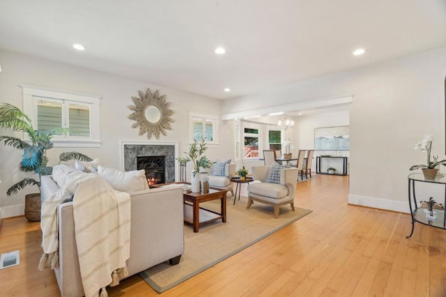 living room with a high end fireplace, light hardwood / wood-style flooring, and a chandelier