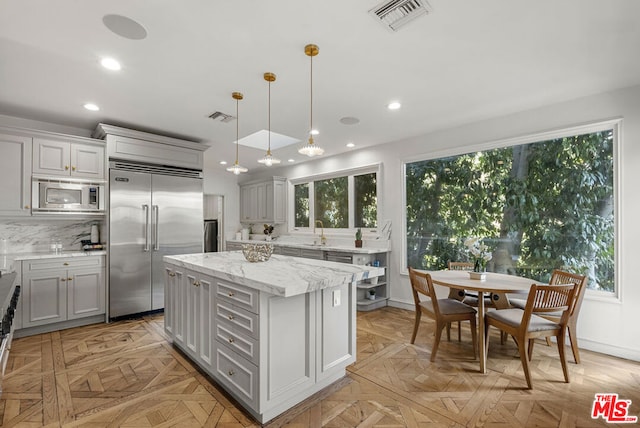 kitchen with a kitchen island, decorative light fixtures, gray cabinetry, built in appliances, and light stone countertops