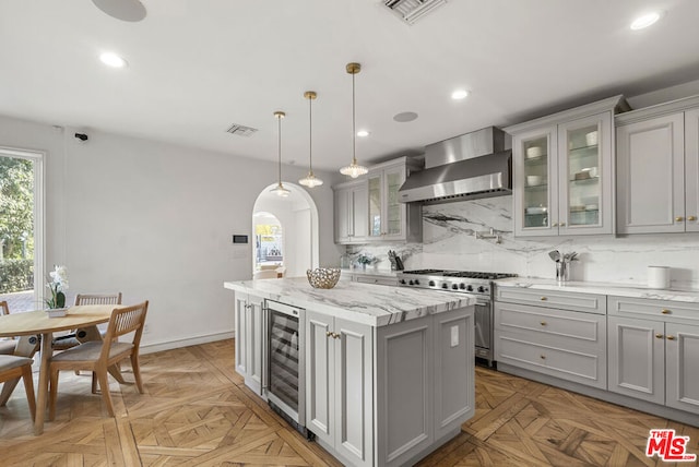 kitchen featuring wall chimney range hood, gray cabinets, high end stainless steel range oven, a center island, and beverage cooler