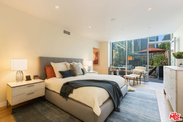 bedroom with expansive windows, access to outside, and light hardwood / wood-style flooring