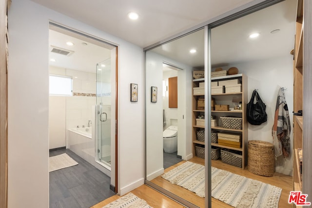 bathroom with wood-type flooring, shower with separate bathtub, and toilet