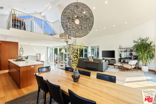 dining room featuring beam ceiling, a towering ceiling, and light hardwood / wood-style floors