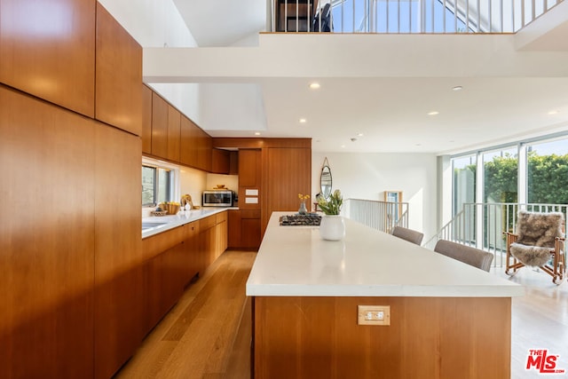 kitchen featuring appliances with stainless steel finishes, a towering ceiling, a spacious island, expansive windows, and light hardwood / wood-style flooring