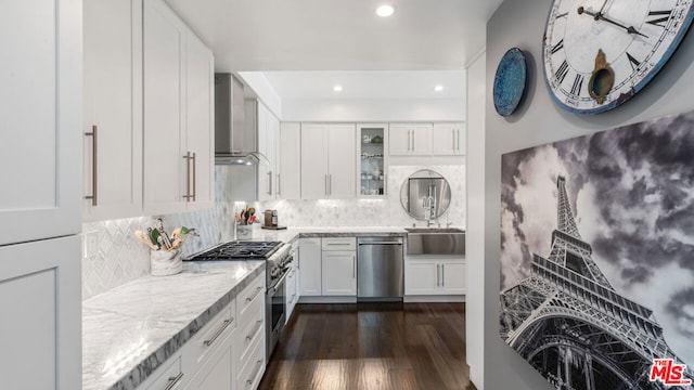 kitchen with appliances with stainless steel finishes, dark hardwood / wood-style flooring, white cabinets, light stone countertops, and wall chimney range hood