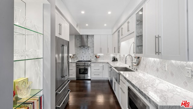 kitchen with dark wood-type flooring, white cabinetry, high end appliances, light stone counters, and wall chimney exhaust hood