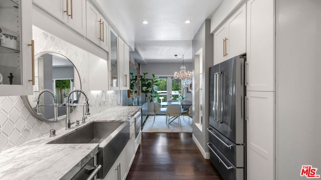 kitchen featuring high end fridge, sink, light stone counters, white cabinets, and backsplash