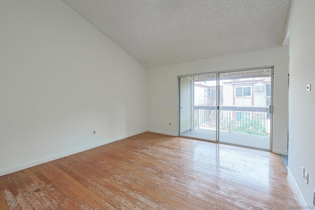 empty room with vaulted ceiling, light hardwood / wood-style flooring, and a textured ceiling