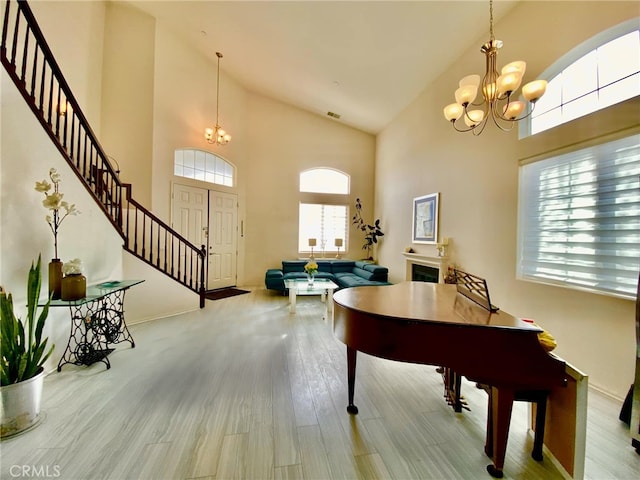 rec room featuring light wood finished floors, a fireplace, high vaulted ceiling, and a notable chandelier