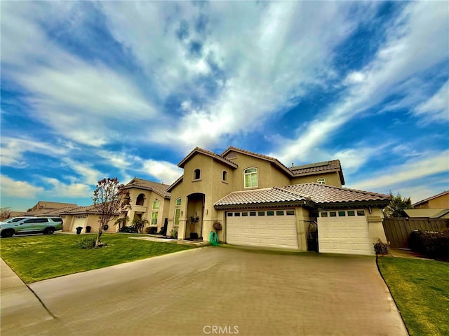 mediterranean / spanish-style home featuring concrete driveway, stucco siding, a tiled roof, an attached garage, and a front yard