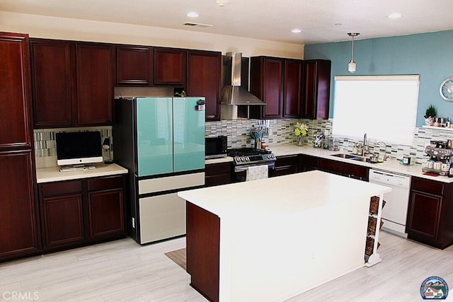 kitchen with white appliances, hanging light fixtures, light countertops, wall chimney range hood, and a sink