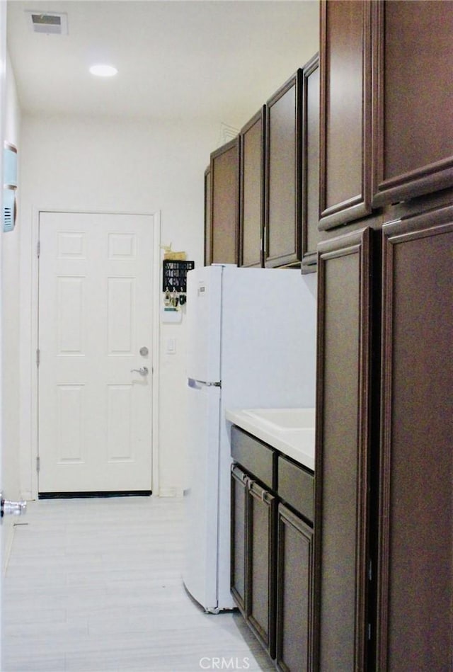 kitchen featuring dark brown cabinetry, visible vents, light wood-style floors, light countertops, and freestanding refrigerator