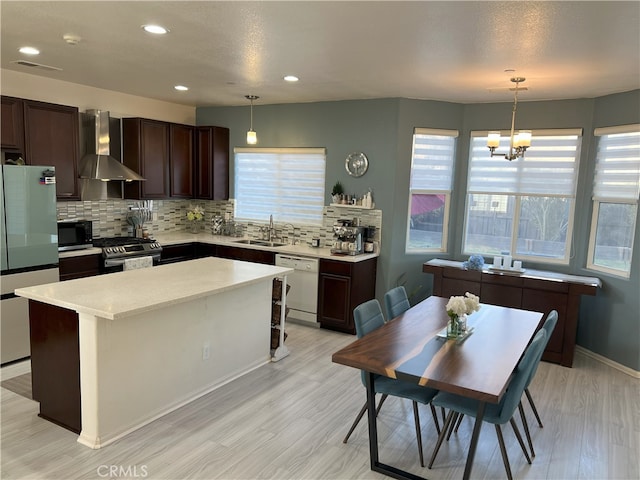 kitchen featuring freestanding refrigerator, pendant lighting, dishwasher, and wall chimney range hood