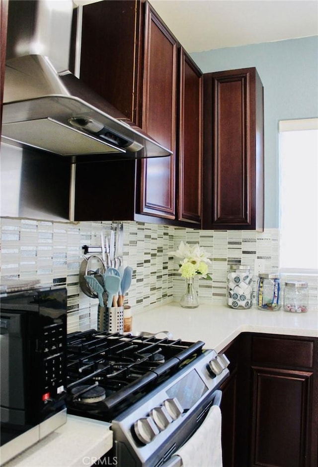 kitchen featuring gas range, light countertops, dark brown cabinets, wall chimney range hood, and backsplash