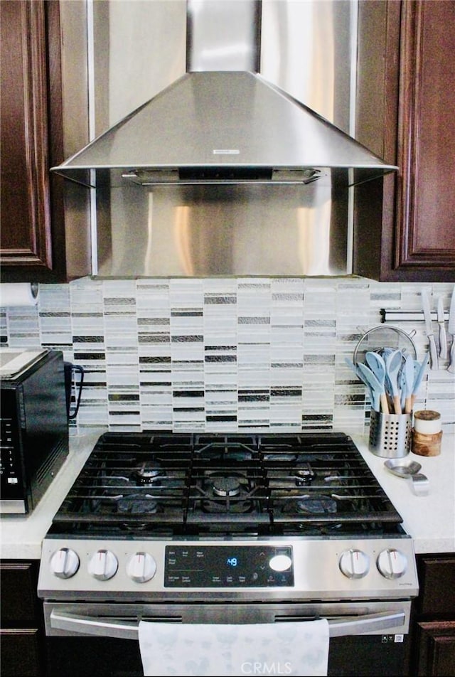 kitchen featuring gas range, wall chimney exhaust hood, light countertops, and decorative backsplash