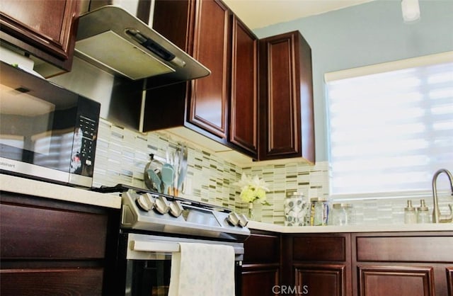 kitchen with under cabinet range hood, stainless steel appliances, a sink, light countertops, and decorative backsplash