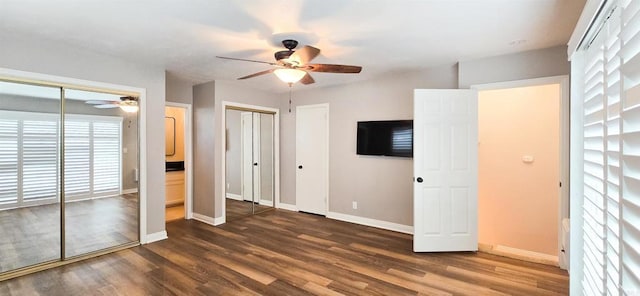 unfurnished bedroom with baseboards, two closets, wood finished floors, and a ceiling fan